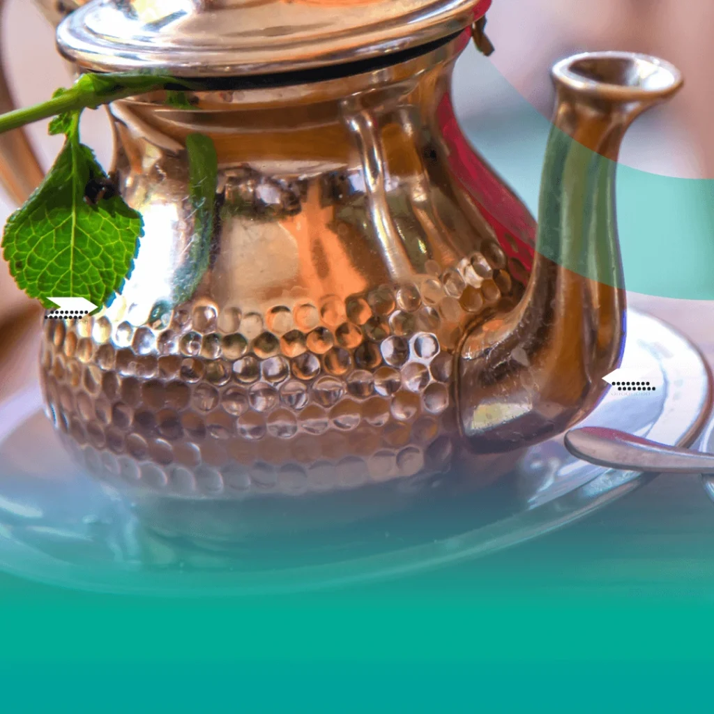 Traditional Moroccan copper teapot with a hammered design, served with fresh mint leaves on a decorative plate.