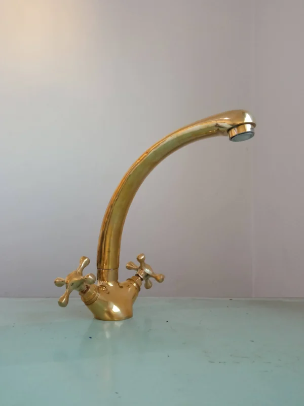 A polished brass kitchen faucet with dual handles and a curved spout, ideal for modern and classic kitchen designs.