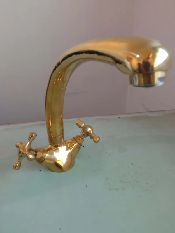 A polished brass kitchen faucet with dual handles and a curved spout, ideal for modern and classic kitchen designs.