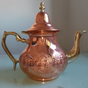 Traditional Moroccan copper teapot with a hammered design, served with fresh mint leaves on a decorative plate.